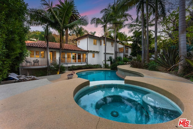 pool at dusk featuring an in ground hot tub