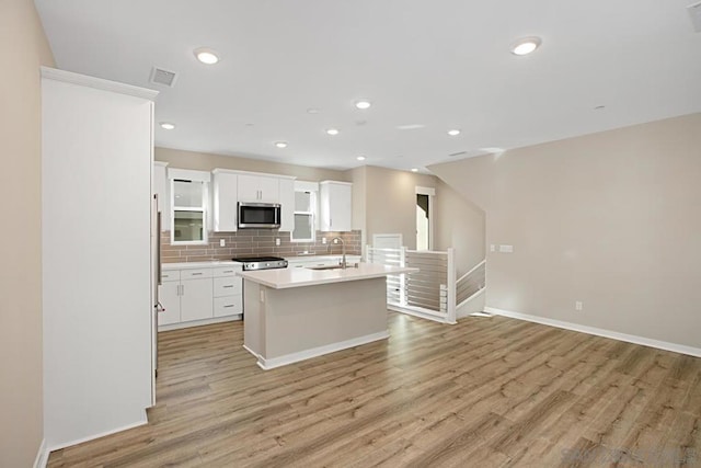 kitchen with backsplash, a kitchen island with sink, light wood-type flooring, white cabinets, and sink