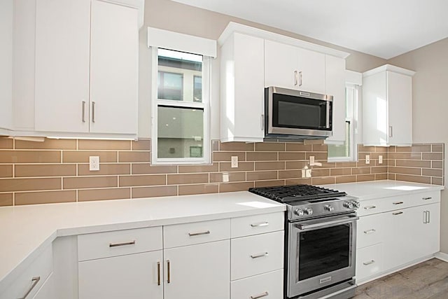 kitchen with white cabinets, backsplash, appliances with stainless steel finishes, and light hardwood / wood-style flooring