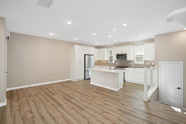 kitchen featuring light hardwood / wood-style floors, a kitchen island, decorative backsplash, appliances with stainless steel finishes, and white cabinets