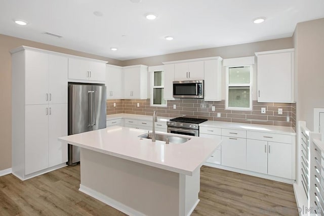 kitchen with white cabinetry, premium appliances, an island with sink, light wood-type flooring, and sink