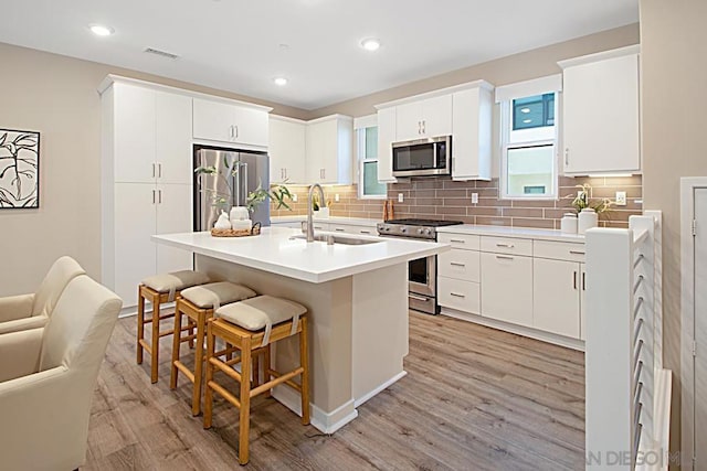 kitchen with a kitchen bar, stainless steel appliances, an island with sink, sink, and light hardwood / wood-style flooring