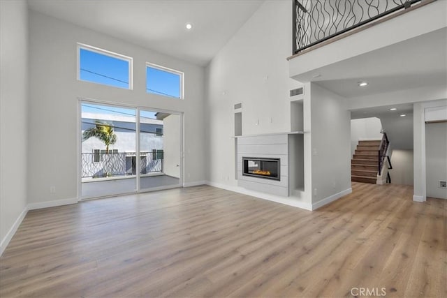 unfurnished living room featuring light wood-type flooring and a towering ceiling