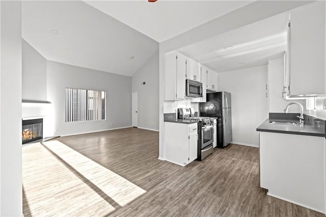 kitchen with appliances with stainless steel finishes, sink, hardwood / wood-style floors, white cabinetry, and lofted ceiling