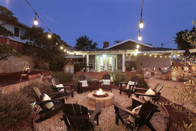 patio terrace at dusk with area for grilling, an outdoor kitchen, and a fire pit