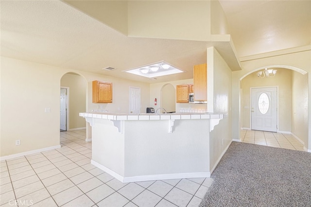 kitchen featuring tile countertops, an inviting chandelier, light tile patterned floors, kitchen peninsula, and a breakfast bar area