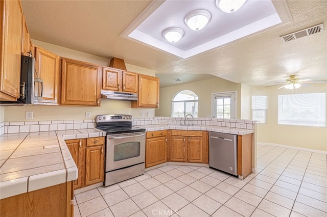 kitchen featuring kitchen peninsula, appliances with stainless steel finishes, a textured ceiling, and tile counters