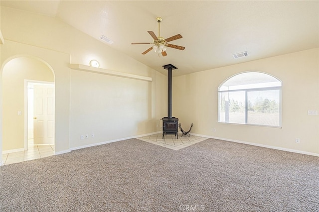 unfurnished living room featuring light colored carpet, a wood stove, ceiling fan, and lofted ceiling