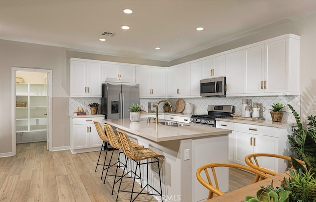 kitchen featuring stainless steel appliances, sink, white cabinets, light hardwood / wood-style floors, and an island with sink