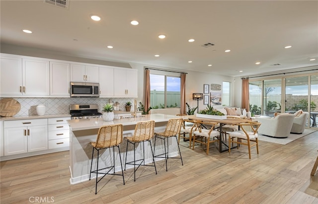 kitchen with a center island with sink, white cabinets, stainless steel appliances, and light hardwood / wood-style flooring