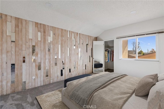 carpeted bedroom with a textured ceiling, a walk in closet, a closet, wood walls, and lofted ceiling