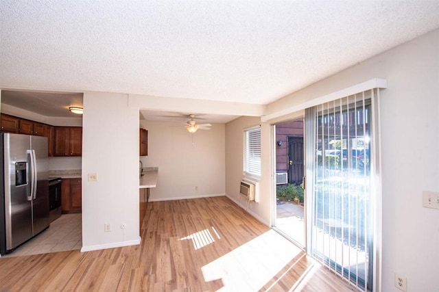 kitchen with light wood-type flooring, ceiling fan, stainless steel fridge, a wall mounted air conditioner, and a textured ceiling