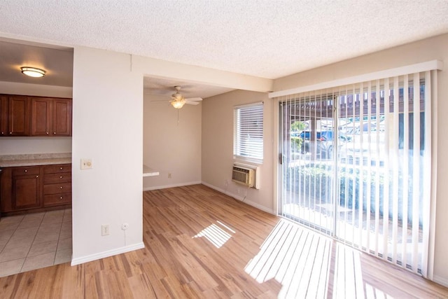 unfurnished living room with an AC wall unit, a textured ceiling, ceiling fan, and light hardwood / wood-style flooring