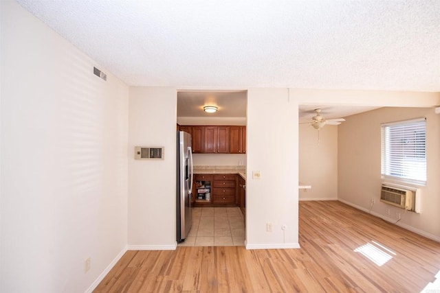 interior space featuring ceiling fan, a wall mounted AC, light wood-type flooring, and a textured ceiling