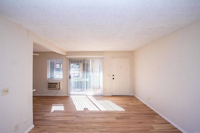 unfurnished room featuring a textured ceiling, a wall mounted AC, and light wood-type flooring