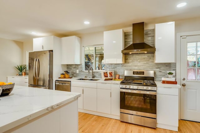 kitchen with white cabinets, appliances with stainless steel finishes, sink, and wall chimney range hood