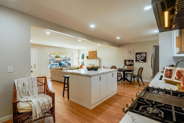 kitchen with stainless steel refrigerator, a kitchen breakfast bar, a center island, light hardwood / wood-style floors, and white cabinets