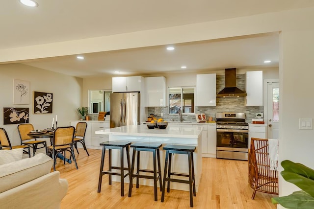 kitchen with light hardwood / wood-style flooring, stainless steel appliances, white cabinets, a kitchen island, and wall chimney exhaust hood