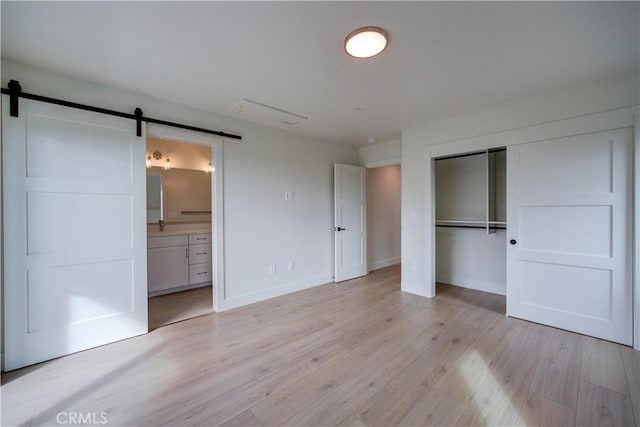 unfurnished bedroom featuring connected bathroom, a barn door, a closet, and light hardwood / wood-style floors