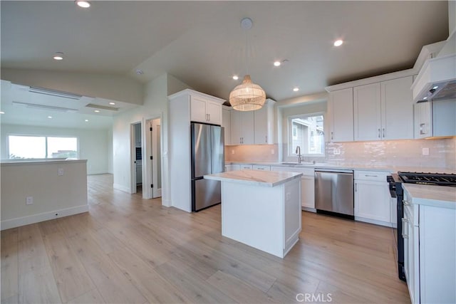 kitchen featuring white cabinetry, decorative light fixtures, vaulted ceiling, a kitchen island, and appliances with stainless steel finishes