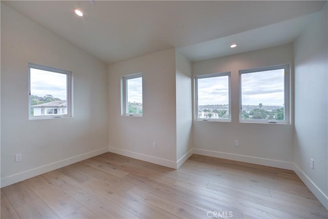 spare room with a wealth of natural light, light hardwood / wood-style floors, and lofted ceiling