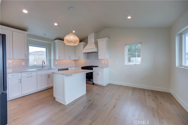 kitchen featuring stainless steel range with gas cooktop, white cabinetry, light wood-type flooring, and custom range hood