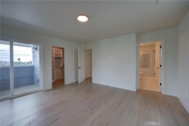 unfurnished bedroom featuring light wood-type flooring, ensuite bathroom, a spacious closet, and a closet