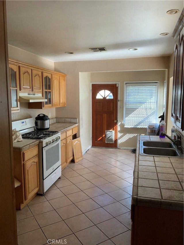 kitchen featuring tile counters, white gas stove, light tile patterned flooring, and sink