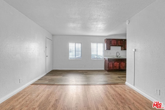 unfurnished living room featuring sink, a textured ceiling, and light wood-type flooring