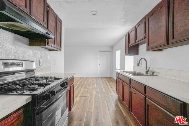 kitchen featuring a textured ceiling, light hardwood / wood-style flooring, stainless steel range with gas cooktop, and sink