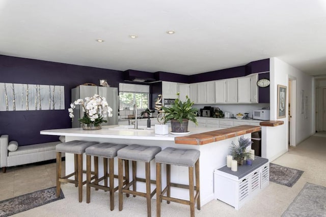 kitchen with a kitchen island, sink, white cabinetry, a kitchen breakfast bar, and stainless steel fridge