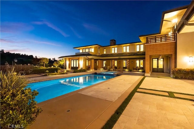 pool at dusk featuring an in ground hot tub and a patio