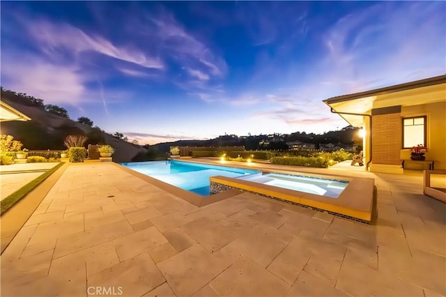 pool at dusk featuring an in ground hot tub and a patio