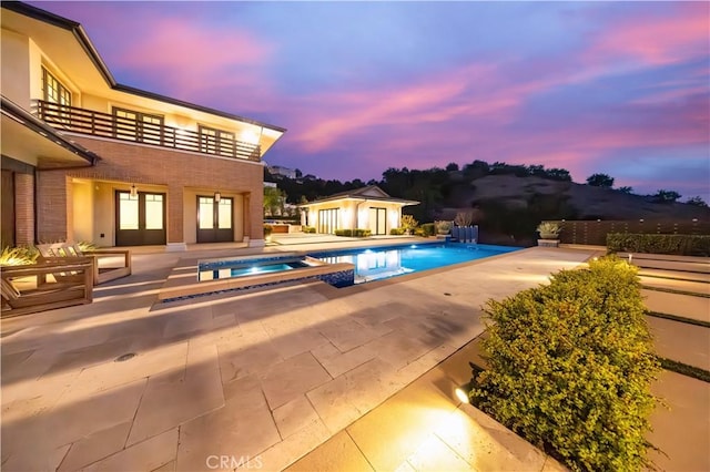 pool at dusk with a patio area and an in ground hot tub