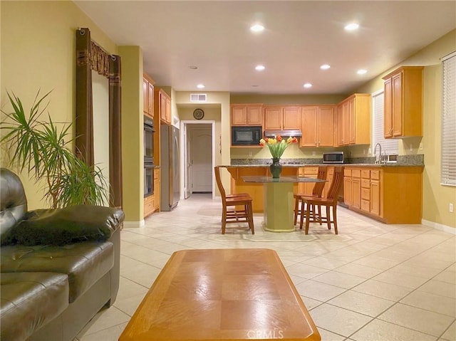 kitchen with a center island, sink, light tile patterned floors, a breakfast bar area, and stainless steel appliances