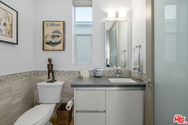 bathroom with vanity, toilet, and tile walls