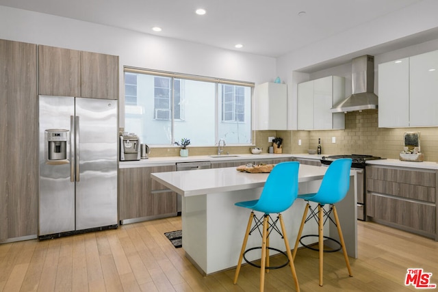 kitchen with a breakfast bar, stainless steel appliances, wall chimney range hood, white cabinets, and a kitchen island