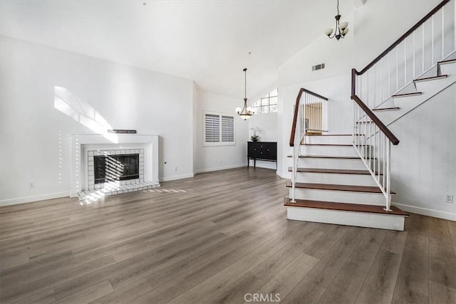 unfurnished living room with a brick fireplace, dark hardwood / wood-style flooring, and an inviting chandelier