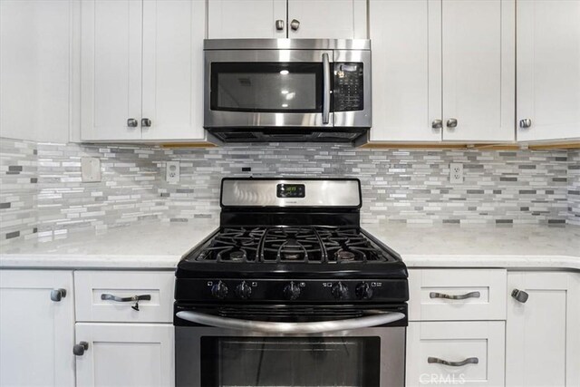 kitchen featuring tasteful backsplash, white cabinetry, light stone countertops, and appliances with stainless steel finishes