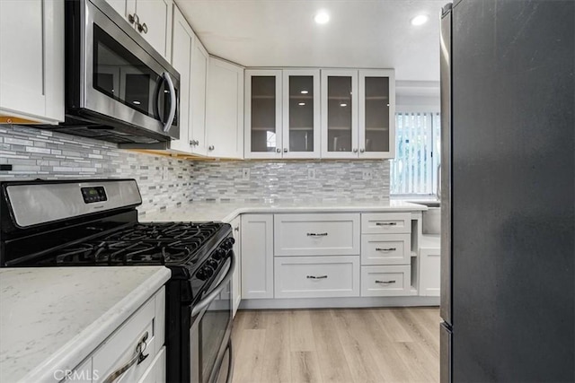 kitchen with light stone countertops, white cabinetry, stainless steel appliances, and light wood-type flooring