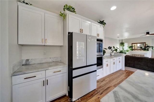 kitchen featuring white cabinets, light hardwood / wood-style flooring, ceiling fan, light stone counters, and stainless steel double oven