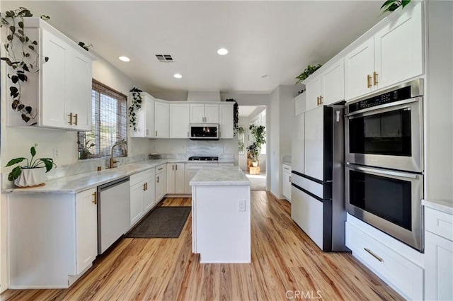 kitchen featuring white cabinets, a center island, stainless steel appliances, and light hardwood / wood-style flooring