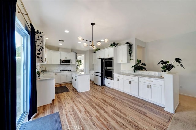 kitchen with appliances with stainless steel finishes, light wood-type flooring, decorative light fixtures, white cabinets, and a center island