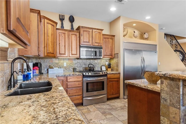 kitchen with light stone countertops, appliances with stainless steel finishes, decorative backsplash, and sink