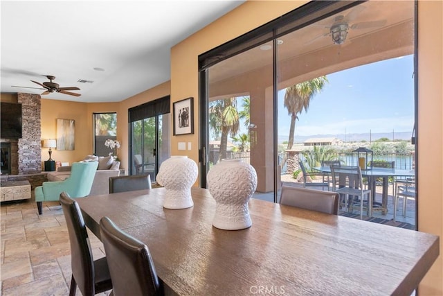 dining space featuring a fireplace, a water view, and ceiling fan