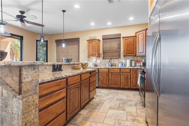 kitchen featuring decorative backsplash, appliances with stainless steel finishes, light stone countertops, sink, and hanging light fixtures