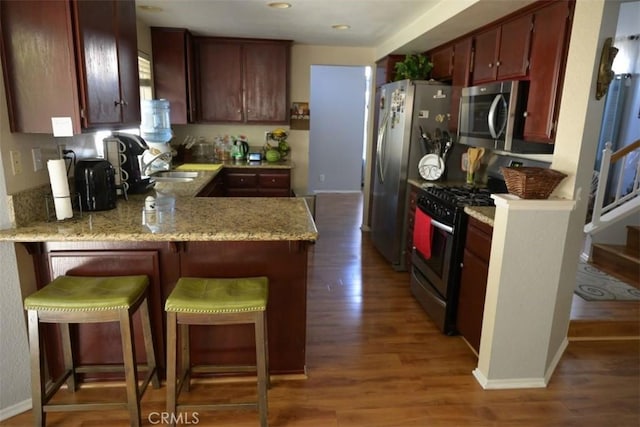 kitchen with a breakfast bar, dark wood-type flooring, sink, appliances with stainless steel finishes, and kitchen peninsula