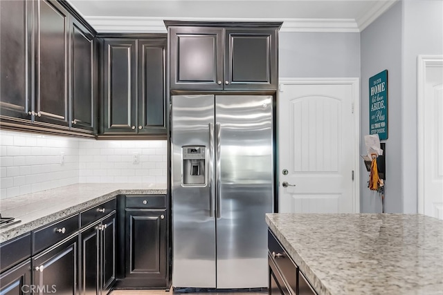 kitchen with stainless steel refrigerator with ice dispenser, backsplash, light stone counters, ornamental molding, and dark brown cabinetry