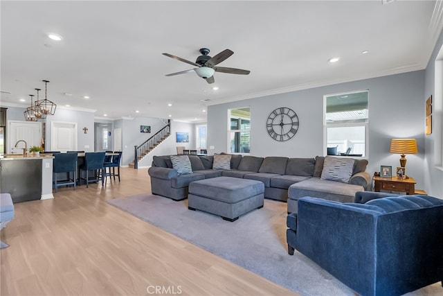 living room with ceiling fan with notable chandelier, light hardwood / wood-style flooring, and crown molding