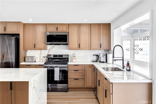 kitchen featuring backsplash, light wood-type flooring, light stone counters, stainless steel appliances, and sink